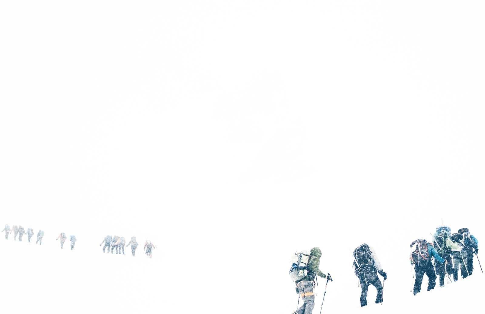 A line of climbers boot packing up a snow slope in a whiteout